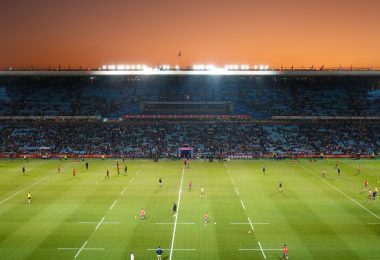 Exciting rugby game unfolding under stunning sunset in large stadium.