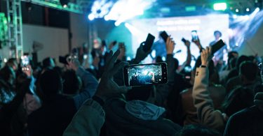 Lively crowd capturing concert moments on smartphones, vibrant lights create dynamic atmosphere.