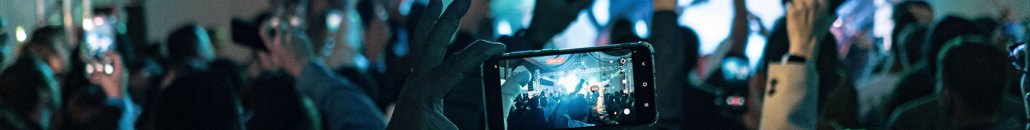Lively crowd capturing concert moments on smartphones, vibrant lights create dynamic atmosphere.
